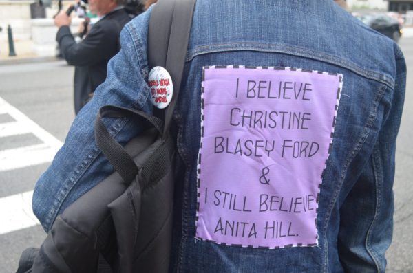 Sign sewn to shirt "I believe christine blasey ford & i still believe anita hill."